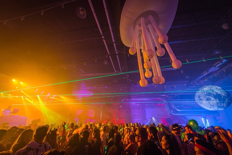 Inflatable jellyfish and moon hang over a packed, laser-lit dance floor