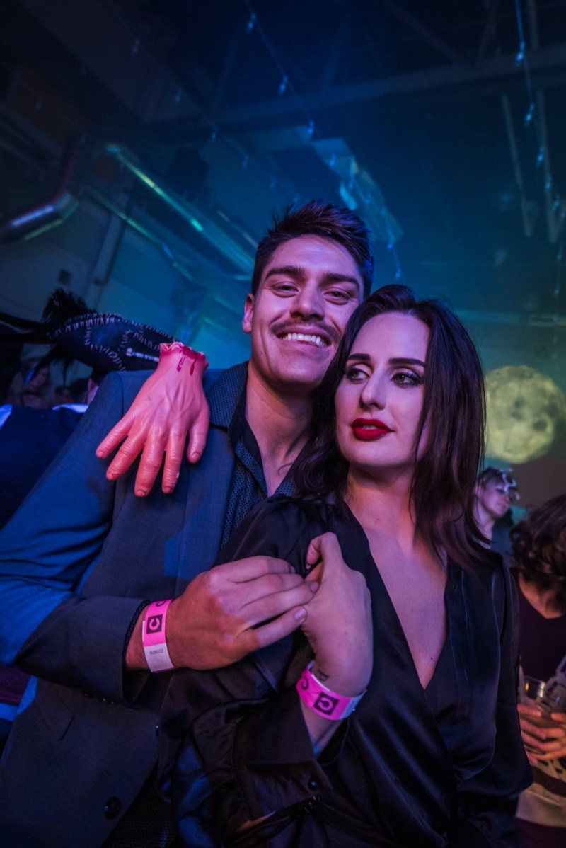 Black-tie couple posing with a severed hand on his shoulder at Coloween 2019 in Colorado
