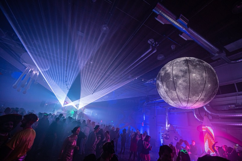 Lasers fan out over a packed floor beneath a glowing moon balloon at Coloween — Denver Halloween nightlife