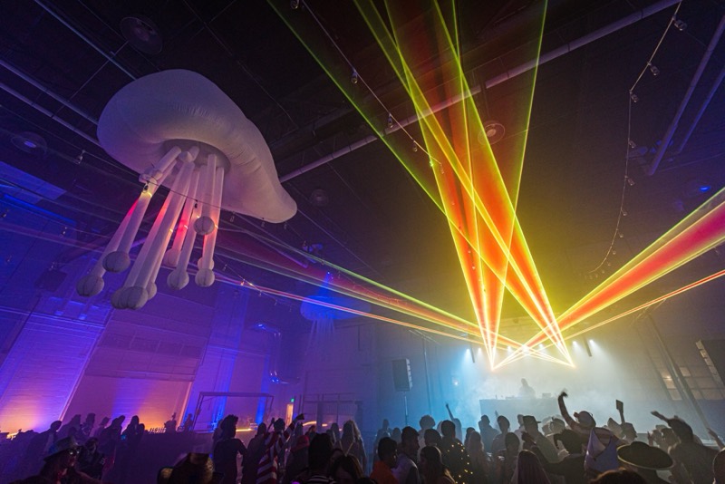 Glowing jellyfish and orange lasers sweep over the costumed crowd at Coloween's Halloween costume party
