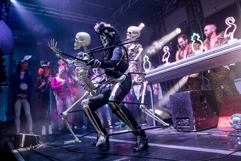 Skeleton puppeteer marching two bone marionettes across the DJ stage