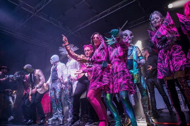 Contest finalists in electric-pink dresses and alien masks own the stage on the dance floor at Coloween 2021