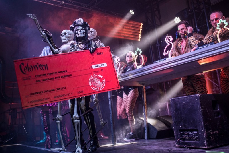 Skeleton-draped winner hoisting the giant costume contest check onstage at Coloween — Denver Halloween nightlife