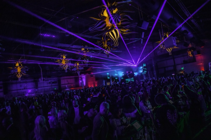 Purple laser fan sweeps the ceiling above a packed dance floor at Coloween, Denver's 21+ Halloween party
