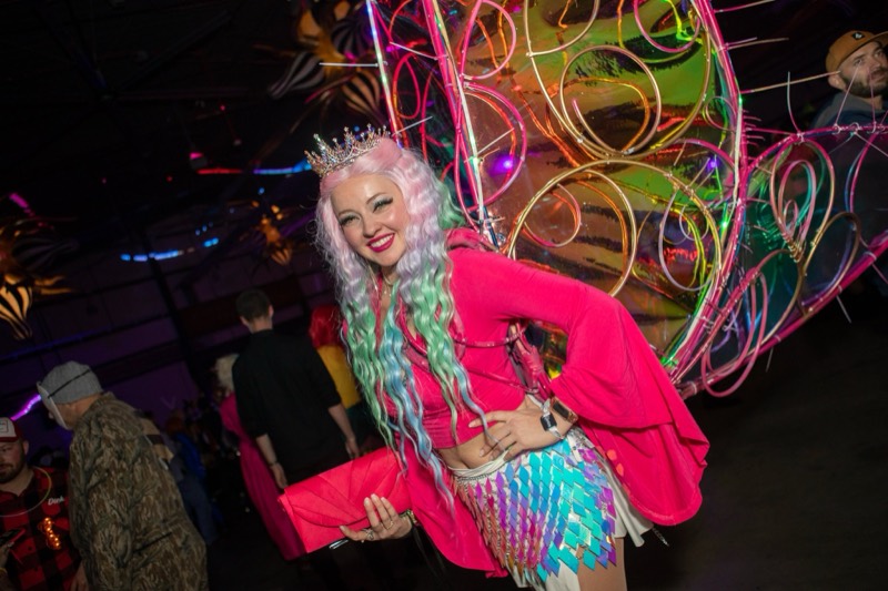Pink-haired queen in a tiara beside an iridescent butterfly sculpture