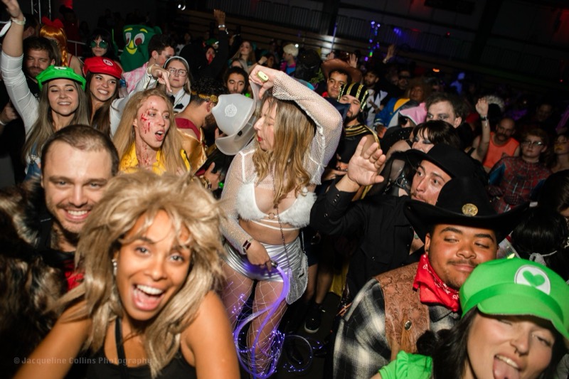 Eighties wigs, plumber caps, and cowboy hats packed on the floor at the adults-only Coloween Halloween event