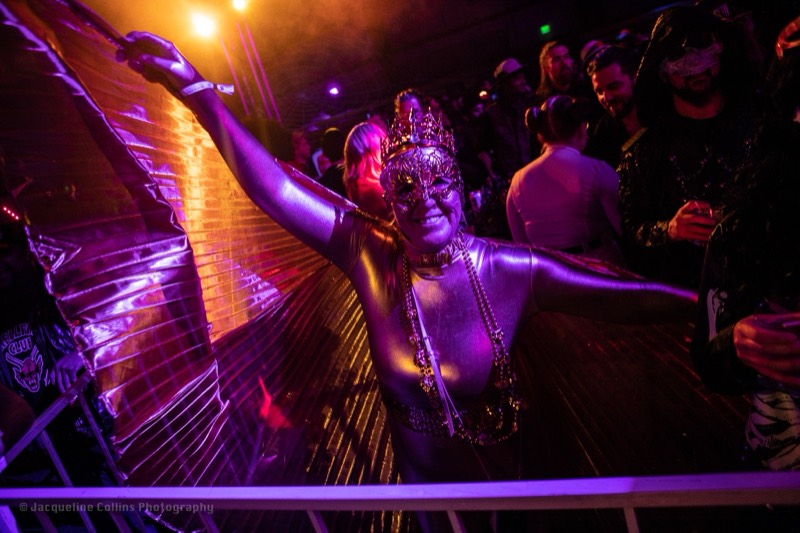Gold-winged dancer spreads her feathers under purple stage light at Coloween's Halloween costume party