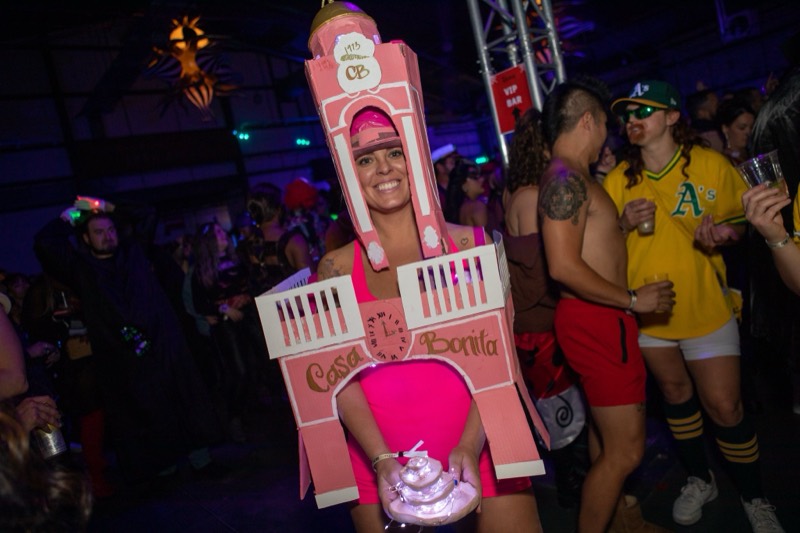 Pink Casa Bonita tower costume holding a plate of lit sopapillas at Colorado's biggest adult Halloween party