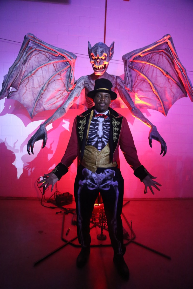 Skeleton ringmaster posing under a giant bat's outstretched wings at Coloween — Denver Halloween nightlife