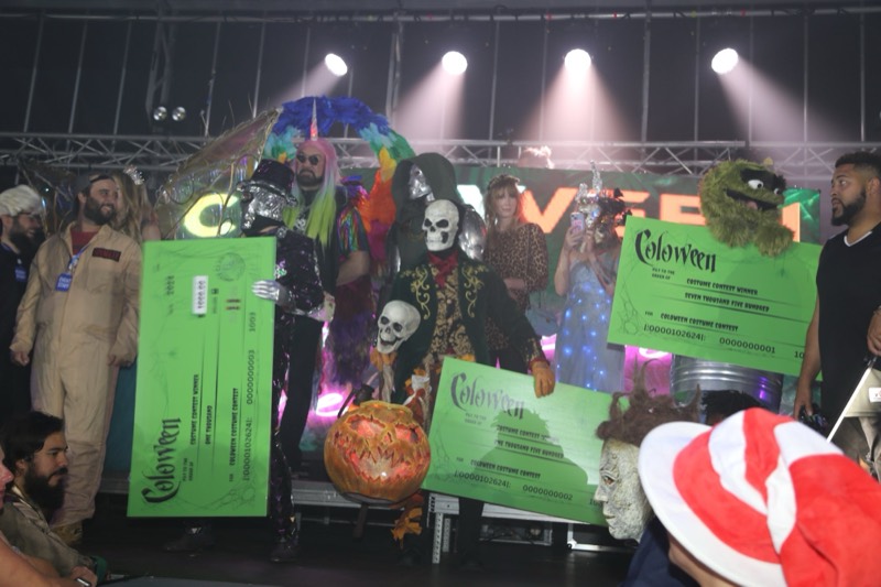 Costume contest winners hoist giant prize checks on stage at the adults-only Coloween Halloween event