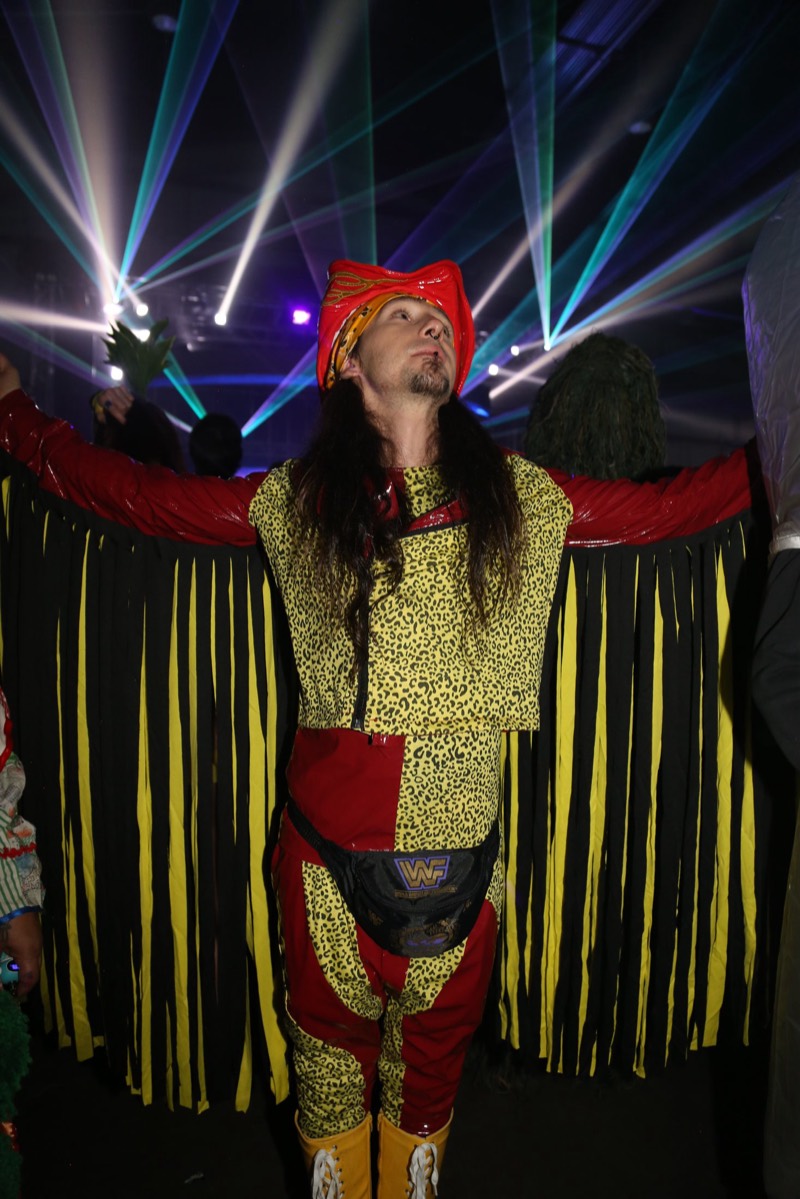 Fringe-winged wrestler costume spread wide under teal lasers at the Coloween costume contest in Denver