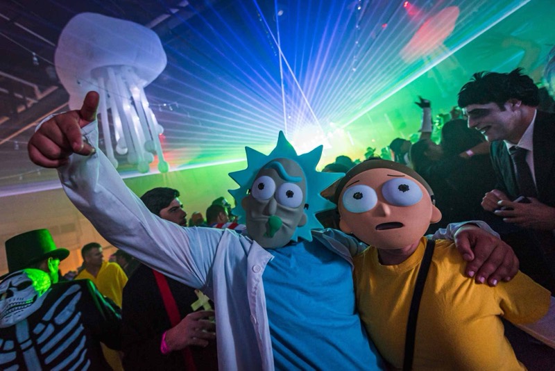 Cartoon scientist and sidekick masks under a fan of lasers at Colorado's biggest adult Halloween party