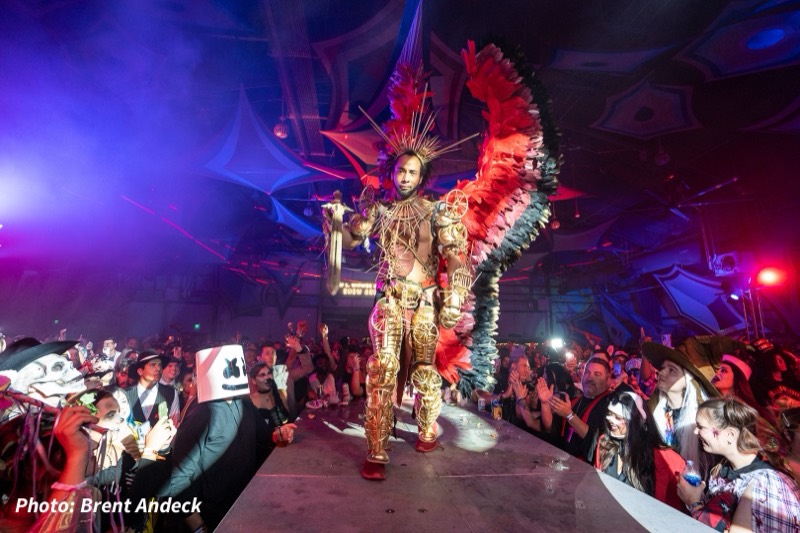 Gold-armored performer with giant red feather wings walking the runway at Coloween 2025 in Colorado