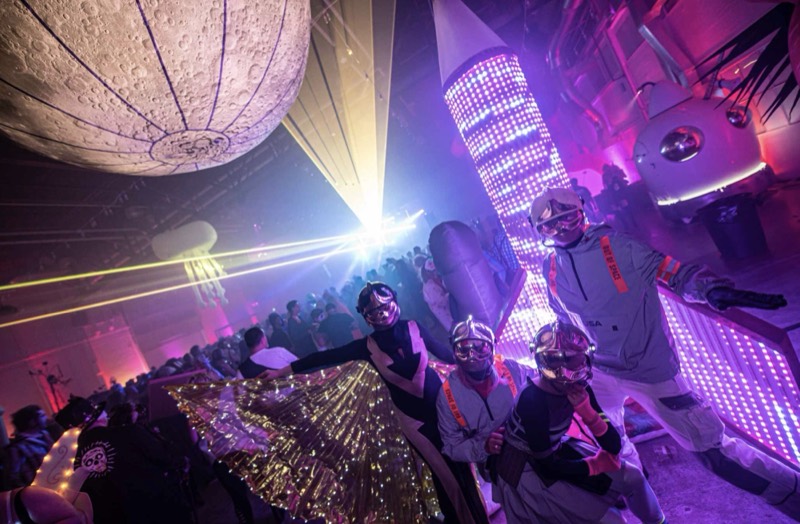 Astronaut crew posing under the inflatable moon and LED rocket at Coloween's Halloween costume party