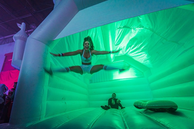 Referee in knee socks mid-split jump inside the glowing bounce castle on the dance floor at Coloween 2025