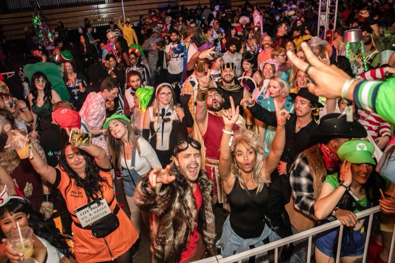 Costumed crowd throwing hands up beneath the balcony rail at the Coloween costume contest in Denver