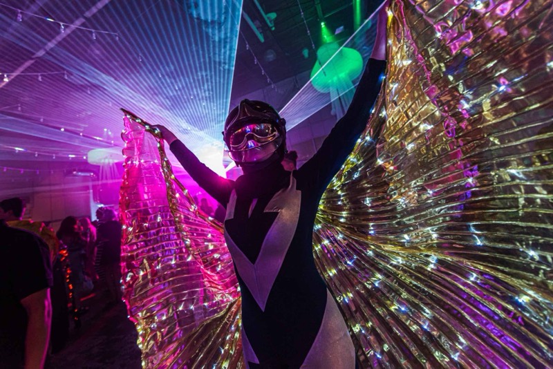 Performer fans out glowing amber LED wings above the crowd at Coloween — Denver Halloween nightlife