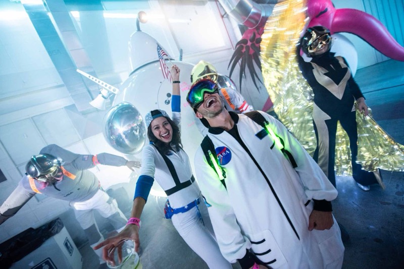 Astronaut crew cheering with a flag beside the rocket photo op on the dance floor at Coloween