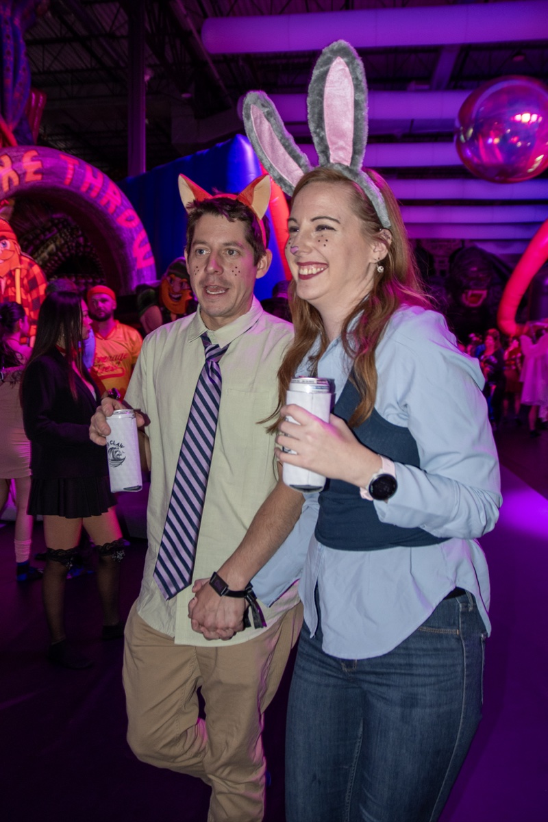 A Zootopia couple laughs hand in hand in the purple glow at Coloween's Halloween costume party