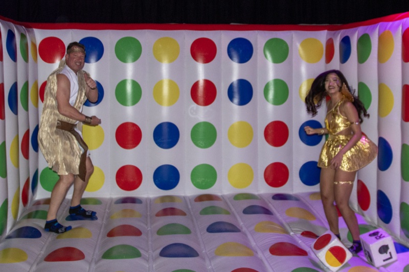 Gold costumes mid-bounce on the giant Twister board, hair airborne at Colorado's biggest adult Halloween party